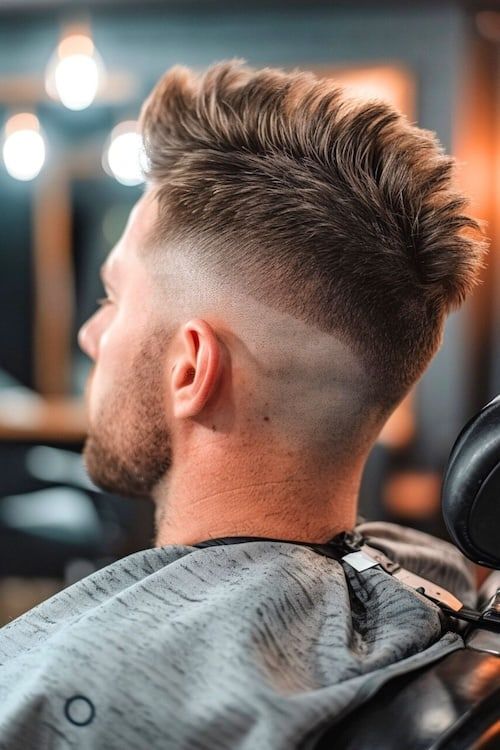 Faux hawk fade haircut on man in barber chair. Toma lateral/trasera.