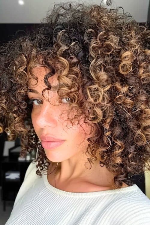Mechas rubio caramelo sobre pelo castaño oscuro rizado y apretado.