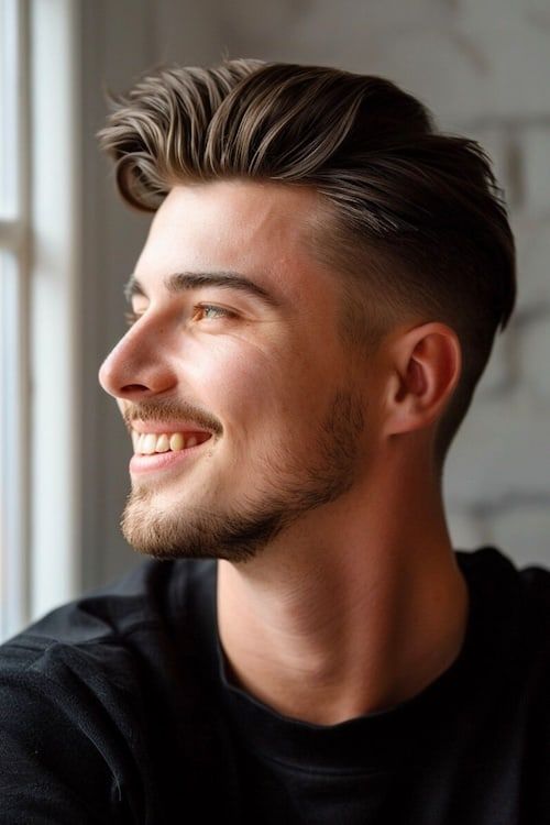 Pompadour con corte de pelo bajo desvanecido en hombre sonriente mirando por una ventana.