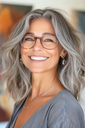 Peinado despeinado de media melena en una mujer sonriente de unos 50 años con el pelo gris y gafas.