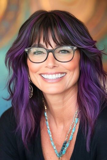 Purple Shaggy Layers with Bangs Peinado en una mujer sonriente de unos 50 años con el pelo morado y negro y gafas.